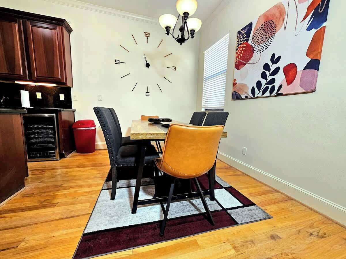 Un comedor con una mesa de madera, sillas negras y anaranjadas, un reloj en la pared y un cuadro abstracto colorido.