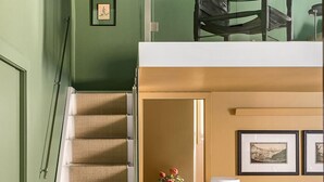 Una escalera conduce a un dormitorio superior con una cama, una lámpara de pie y un sofá amarillo.
