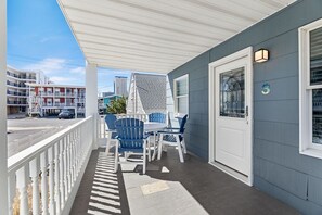 En inglasad veranda med ett vitt räcke, blå Adirondack-stolar och ett bord.