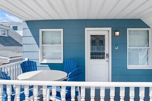 Ett blått hus med en vit dörr, en liten veranda med ett vitt räcke och ett runt bord med blå stolar.