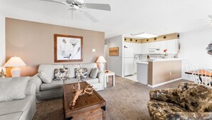 A living room with a sofa, a coffee table, and a patterned armchair. There is a kitchen area in the background with white cabinets and a dining table. - 2 BEDROOM 2 BATH AT ISLAND AT HIDDEN HARBOUR (Ocean City)