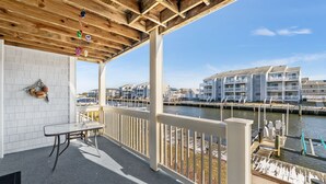 A covered outdoor area with a table and chairs, a railing, and a view of a marina with buildings and boats. - 2 BEDROOM 2 BATH AT ISLAND AT HIDDEN HARBOUR (Ocean City)