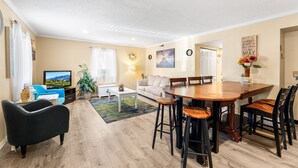 Un salon comprenant un téléviseur, un canapé, une table basse et une table à manger avec des chaises.