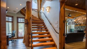 A wooden staircase with a handrail, a stone wall, and a ceiling fan in a room with wooden floors and large windows. - Parabull's Point, Lake Lure, Luxury House with water slide (Lake Lure)