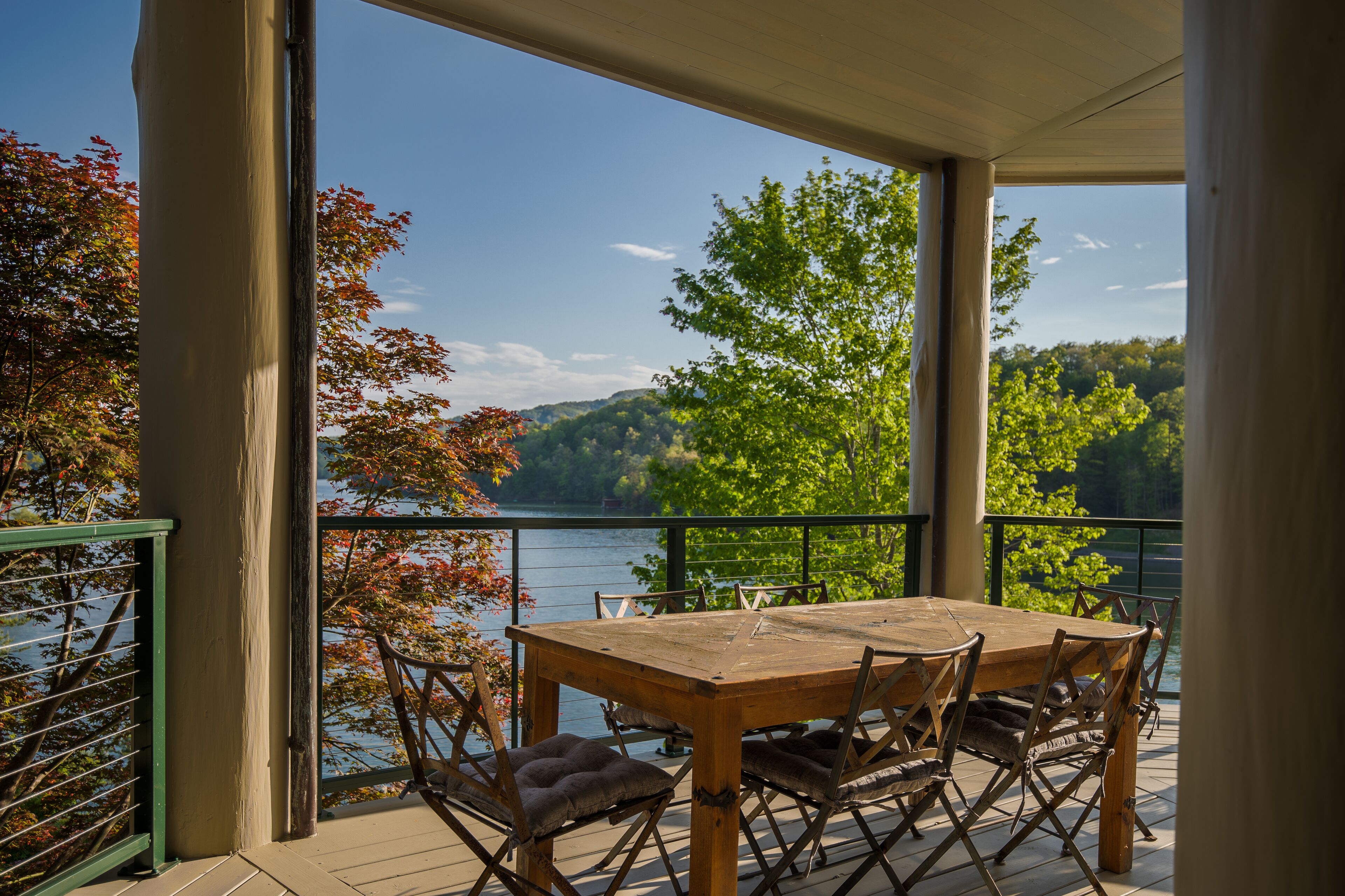 A wooden table and chairs on a balcony with a view of a lake and trees.