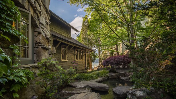 A rustic stone house with a pond, surrounded by lush greenery and a wooden deck. - Parabull's Point, Lake Lure, Luxury House with water slide (Lake Lure)