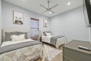 Une chambre avec deux lits, un ventilateur de plafond et un téléviseur.
