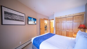 Un dormitorio con cama, un cuadro de un paisaje montañoso, un cuadro de un esquiador y un armario de madera.