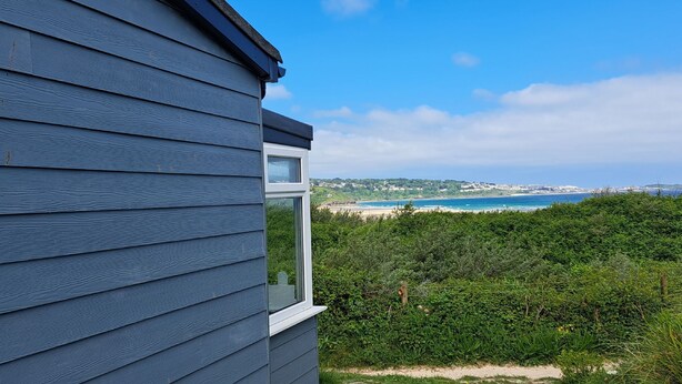 Uitzicht vanuit een raam op een strand en de oceaan, met een huis op de voorgrond.