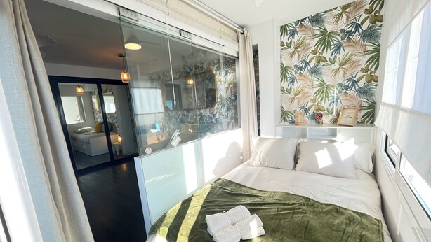 Ein Hotelzimmer mit einem großen Bett, einer Glasschrankwand und tropischem Blattendekor.