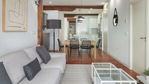 A modern living room with a sofa, a glass coffee table, and a dining area with chairs and a table. - Marina | The Rentals Collection (San Sebastián/Donostia)