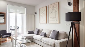 A modern living room with a white sofa, a glass coffee table, and a herringbone-patterned rug. There are abstract art pieces on the wall and a floor lamp. - Marina | The Rentals Collection (San Sebastián/Donostia)