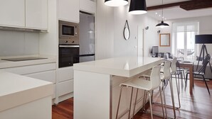 A modern kitchen with white cabinetry, a built-in oven, and a central island with bar stools. - Marina | The Rentals Collection (San Sebastián/Donostia)