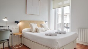 A neatly arranged bedroom with a bed, bedside lamps, a chair, and a window with a view. - Marina | The Rentals Collection (San Sebastián/Donostia)