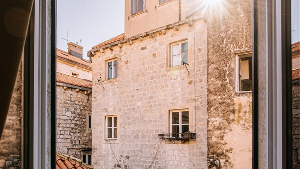 A view through a window of a narrow street with old buildings, a tiled roof, and a clear sky. - Illyria Old Town Apartment by DuHomes (Dubrovnik)