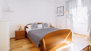A bedroom with a wooden bed, white walls, a nightstand with a lamp, a framed picture on the wall, and a window with sheer curtains. - Illyria Old Town Apartment by DuHomes (Dubrovnik)