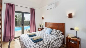 A bedroom with a bed, a nightstand, a lamp, an air conditioner, and a view of a swimming pool. - Villa Argentina - Three Bedroom Villa, Sleeps 6 (Montaña Roja)