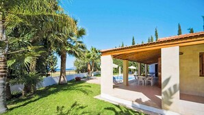 A covered outdoor area with a pool, palm trees, and a view of the sea.