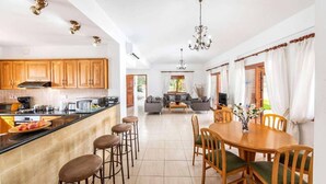 A spacious kitchen with wooden cabinets, a central island with stools, and a dining area with a wooden table and chairs.