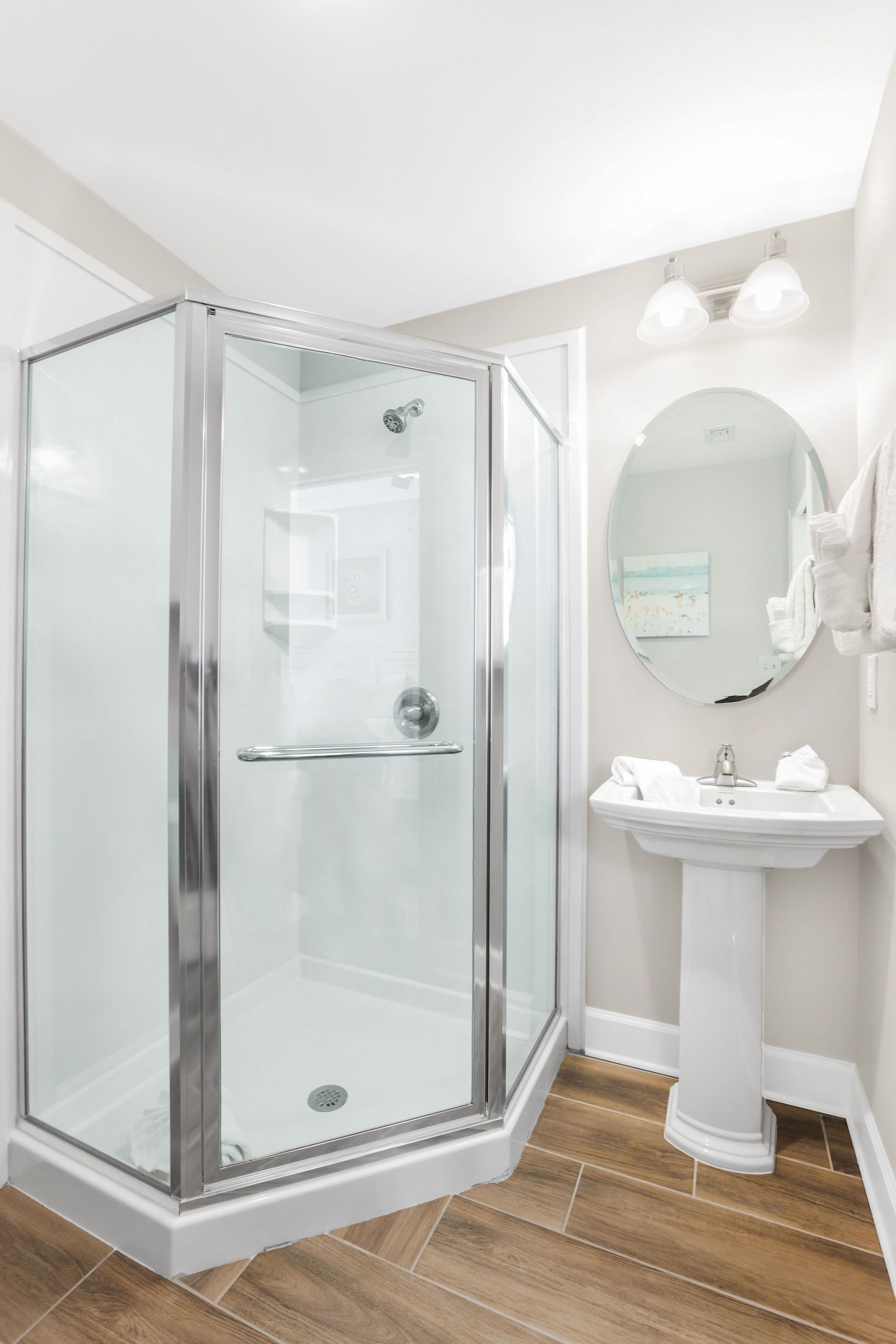 Un baño moderno con ducha de vidrio, lavamanos sobre pedestal y espejo redondo.