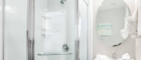 Un baño moderno con ducha de vidrio, lavamanos sobre pedestal y espejo redondo.