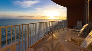 Een balkon met uitzicht op de oceaan bij zonsondergang, met een hekwerk, een paar stoelen en een tafel.