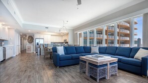 Un vaste espace de vie comprenant un grand canapé d’angle bleu, une table basse et un coin repas avec des meubles en osier.