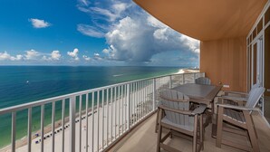 Ein Balkon mit Blick auf den Ozean und den Strand, ein Tisch mit Stühlen und einem Geländer.