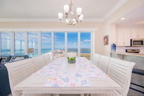 A dining area with a table set for four, large windows, a chandelier, and a view of the ocean.