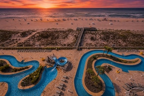 A resort with a large pool area, a water slide, and a beach view.
