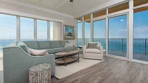 A spacious living room with a view of the ocean, a green sofa, a beige armchair, and a coffee table.