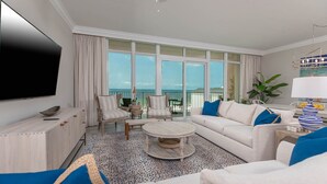 Ein großzügiges Wohnzimmer mit großem Fernseher, bequemen Sitzmöglichkeiten, einem Couchtisch und Meerblick durch große Fenster.