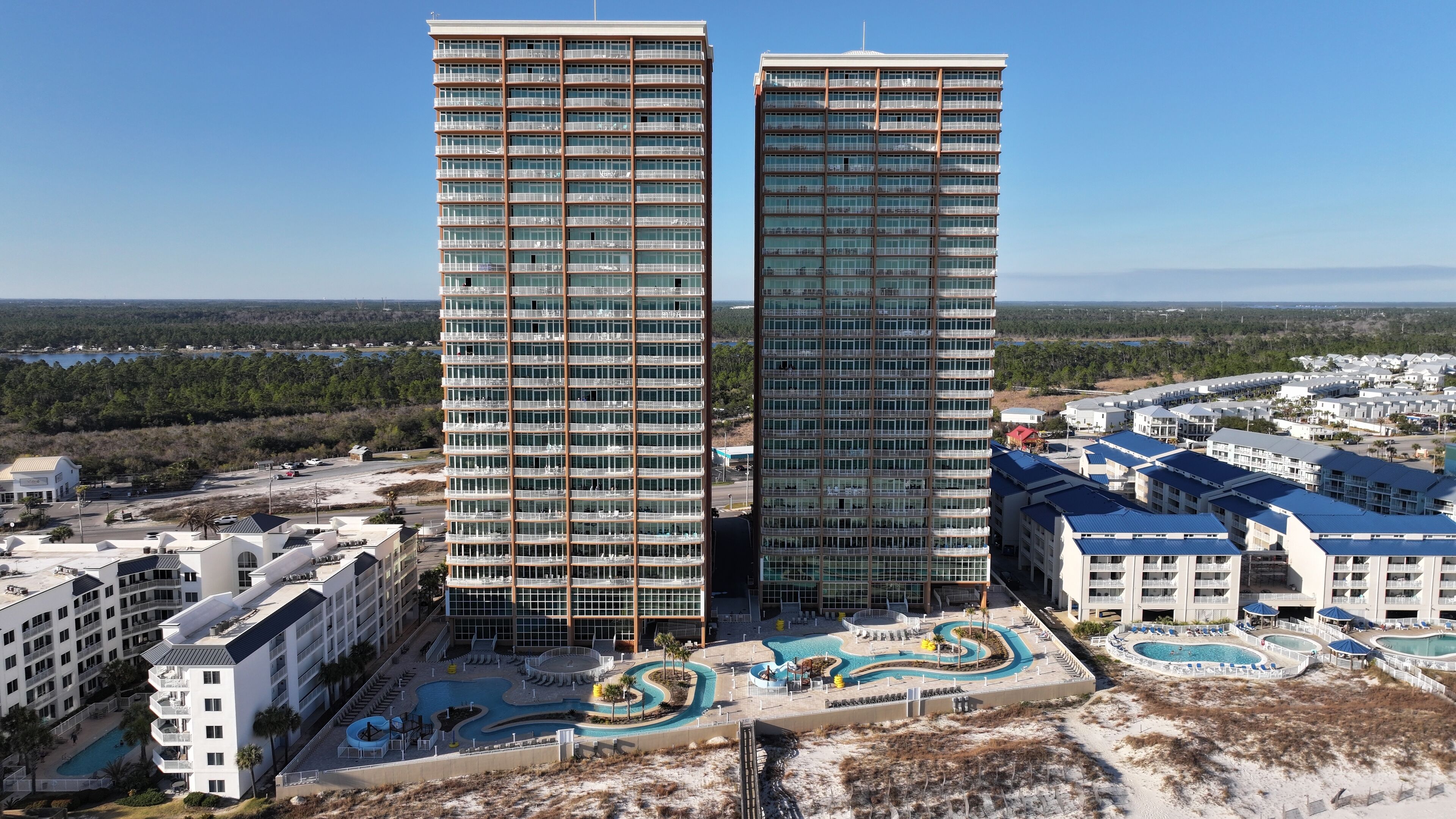 Deux immeubles de grande hauteur dotés de nombreux balcons, un espace piscine avec une piscine au design sinueux, et une vue sur un paysage côtier.