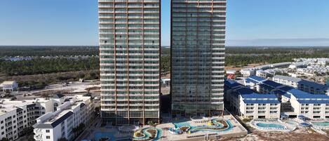 Deux immeubles de grande hauteur dotés de nombreux balcons, un espace piscine avec une piscine au design sinueux, et une vue sur un paysage côtier.