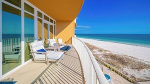 Un balcón con sillas y mesa blancos, con vista a una playa de arena blanca y aguas azules cristalinas.