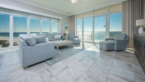 A spacious living room with a large window overlooking the ocean, a ceiling fan, and a view of the beach. - Phoenix Gulf Towers 804  Corner Gulf-Front Escape (Orange Beach)