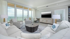 Een ruime woonkamer met een grote flatscreen-tv, een eethoek en een balkon met uitzicht op de oceaan.