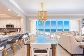 Une cuisine moderne dotée d’un îlot central, un coin repas offrant une vue sur l’océan et un salon avec un canapé et une vue sur la plage.