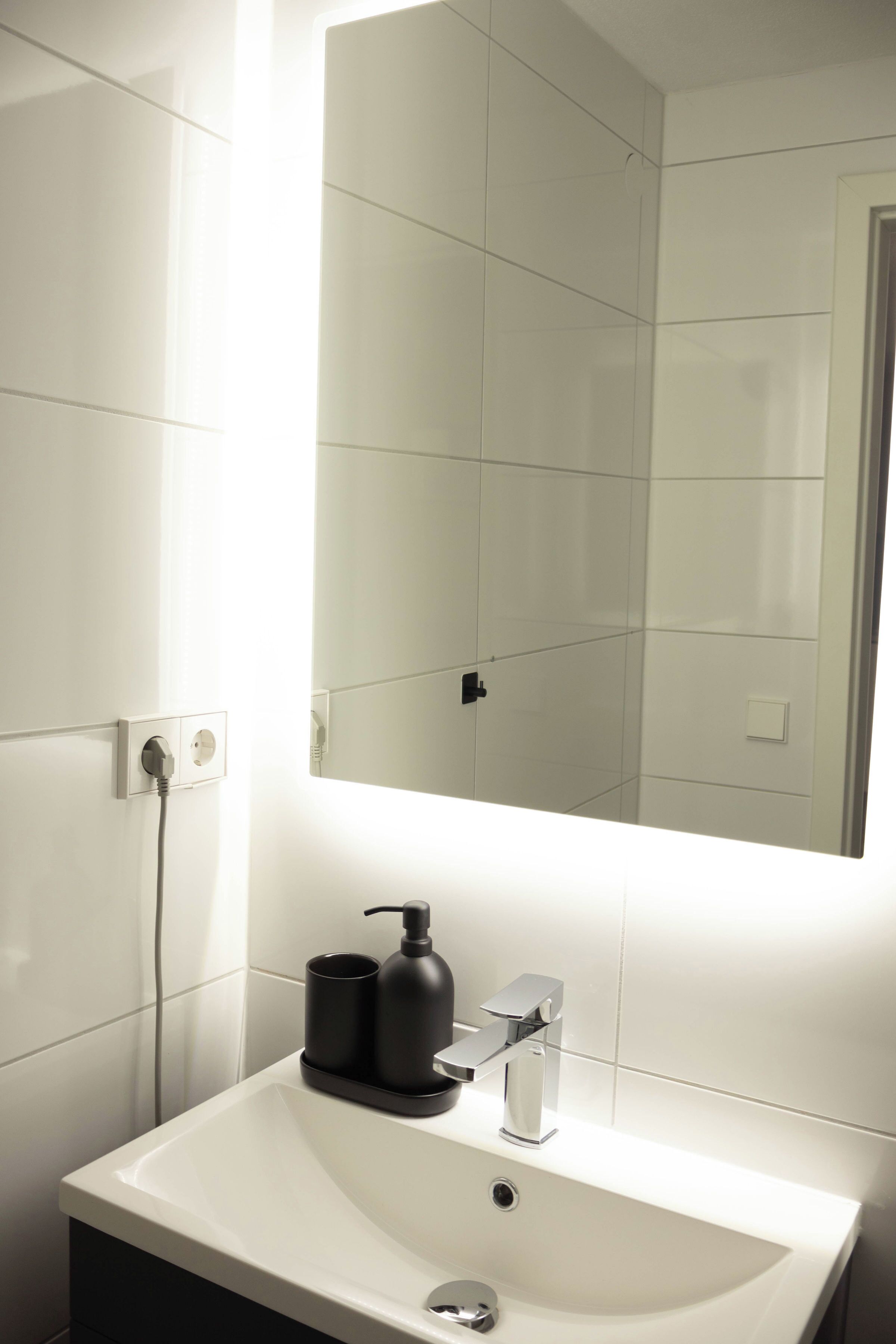 A bathroom with a white sink, a mirror, and a black soap dispenser.