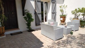 Un patio al aire libre con mobiliario de mimbre, plantas en macetas y una puerta de madera.