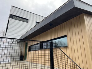 A modern building with a sloped roof, a large window, and a metal fence.