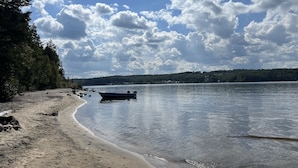 A beach with a boat, calm water, and a forested area in the background. - New construction, This Chalet is ready to enjoy all seasons ! (Saint-Michel-Des-Saints)