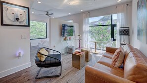 A modern living room with a leather sofa, a black chair, and a wooden coffee table. There is a large window with a view of greenery outside.