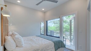 A bedroom with a large bed, a ceiling fan, and a view of a balcony.