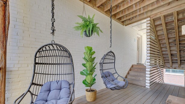 A wooden deck with two hanging chairs and a potted plant.