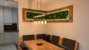 A dining area with a wooden table and cushioned benches, a decorative wall panel, and a hanging light fixture. - Ferienhaus Grundmann - im Allgäu mit Wunderschönem Berg- Seepanorama (Lechbruck am See)