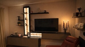 A modern living room with a flat-screen TV, a leather armchair, and a built-in entertainment unit with shelves and a lit-up display. - Ferienhaus Grundmann - im Allgäu mit Wunderschönem Berg- Seepanorama (Lechbruck am See)