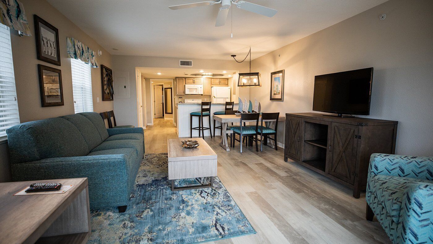 A living room with a sofa, coffee table, TV, and a dining area with chairs and a table.