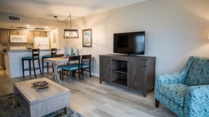 Un espacio habitable compacto con kitchenette, comedor, televisor y un sillón estampado.