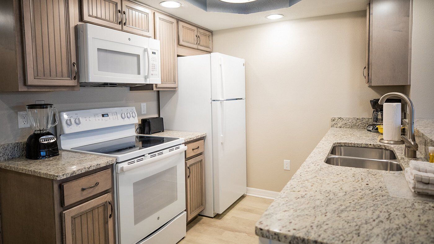 A kitchen with a stove, microwave, refrigerator, granite countertop, and wooden cabinets.